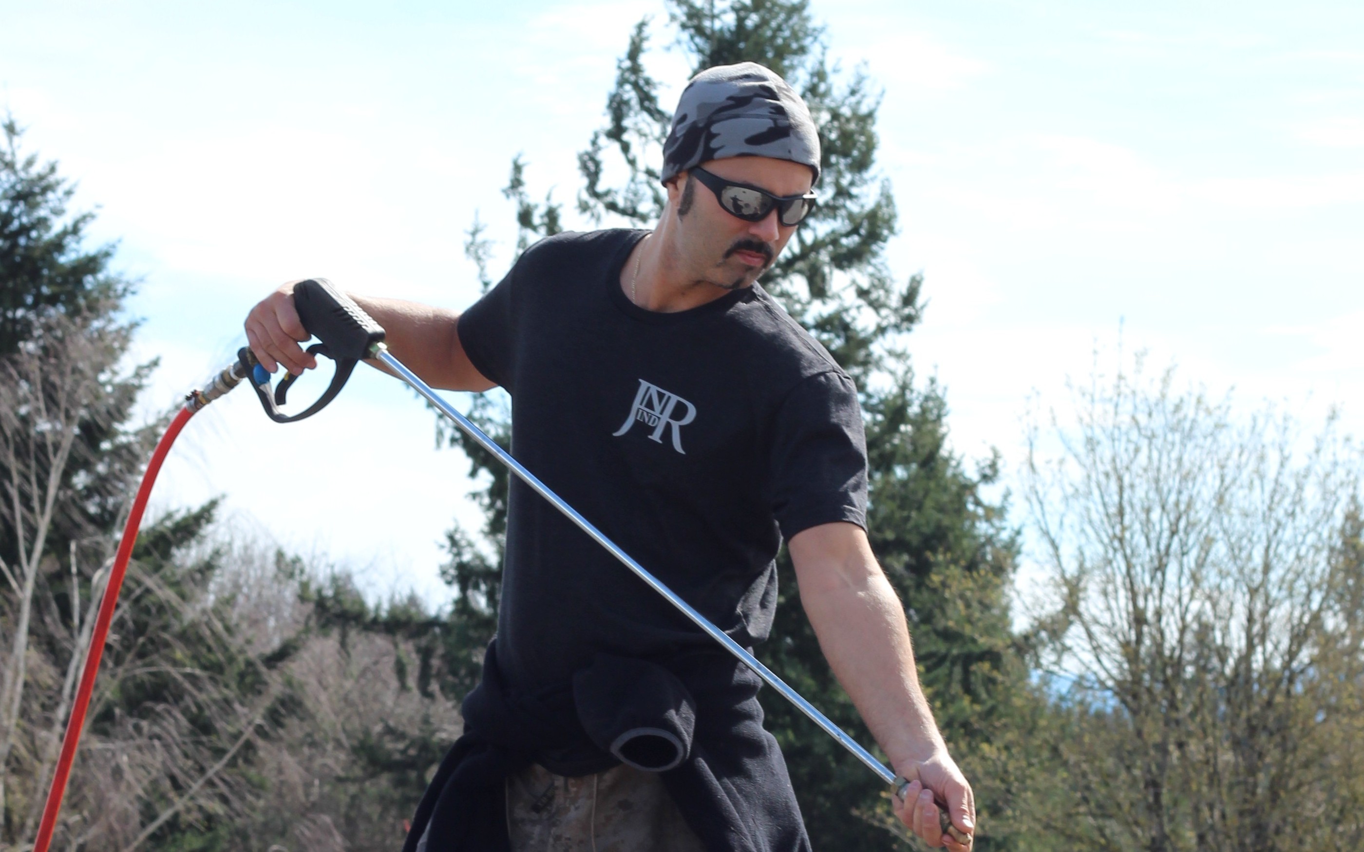 Jesse from JNR Industries applying eco-friendly moss treatment on a Portland roof, spray wand in hand
